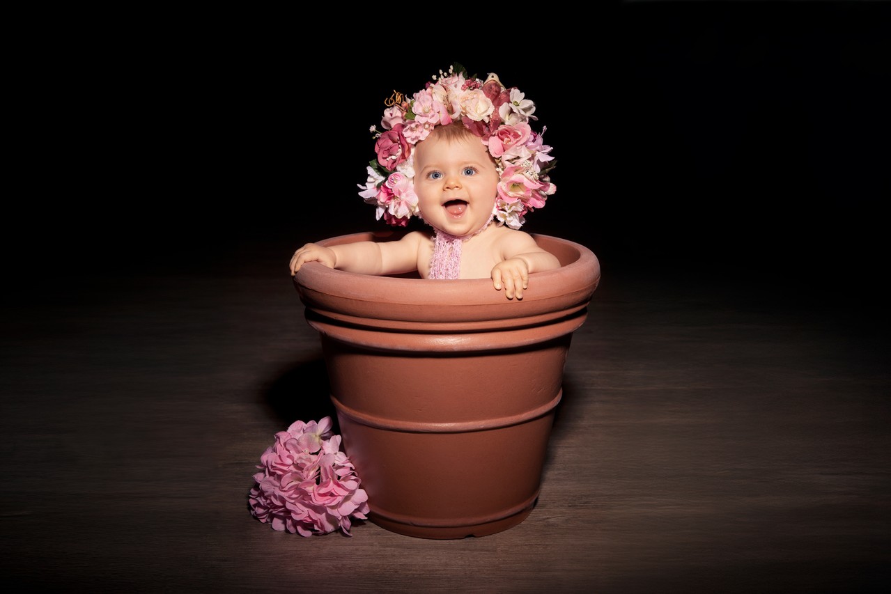 Ein Baby sitzt in einem Blumentopf und lächelt in die Kamera