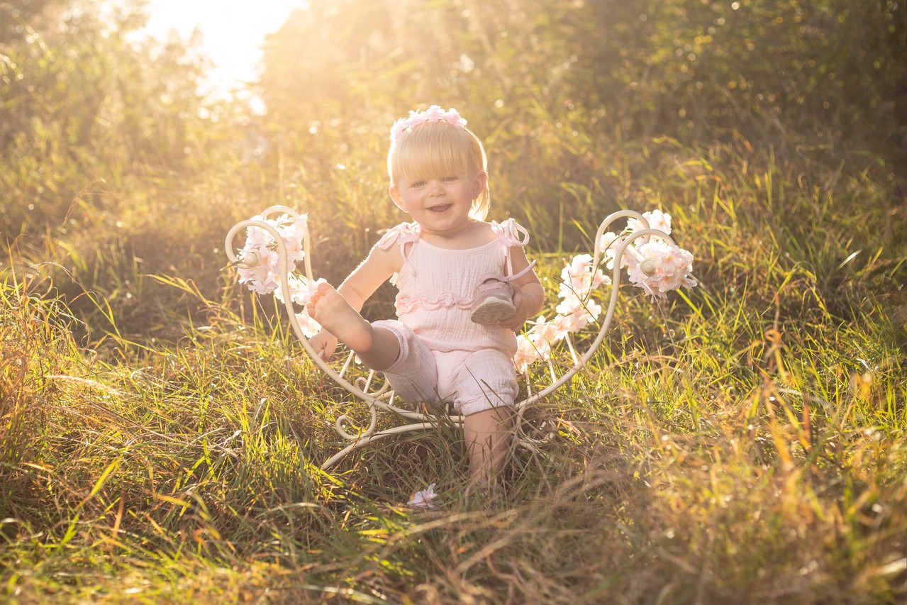 Ein Baby sitzt auf einem weißen Bettgestell auf einem Feld im Sommer