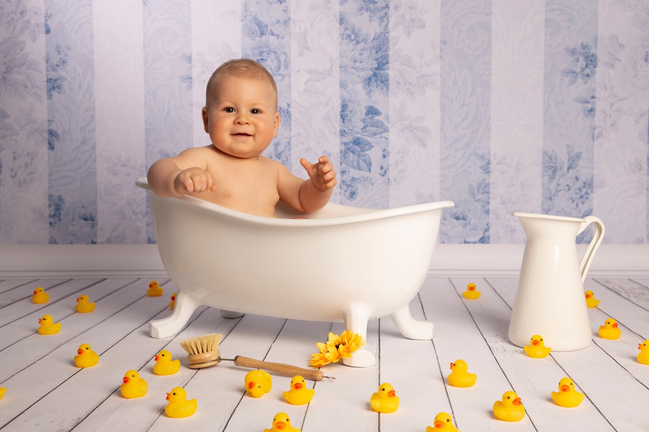 Ein Baby sitzt in einer Badewanne umringt von gelben Quitscheenten