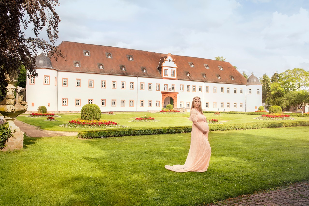 Eine werdende Mutter posiert im Schwangerschaftskleid vor dem Schloss Heusenstamm